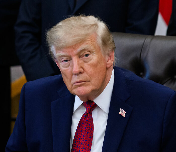 Donald Trump looking forward while seated in a dark blue suit with a red tie. Donald Trump looking forward while seated in a dark blue suit with a red tie.