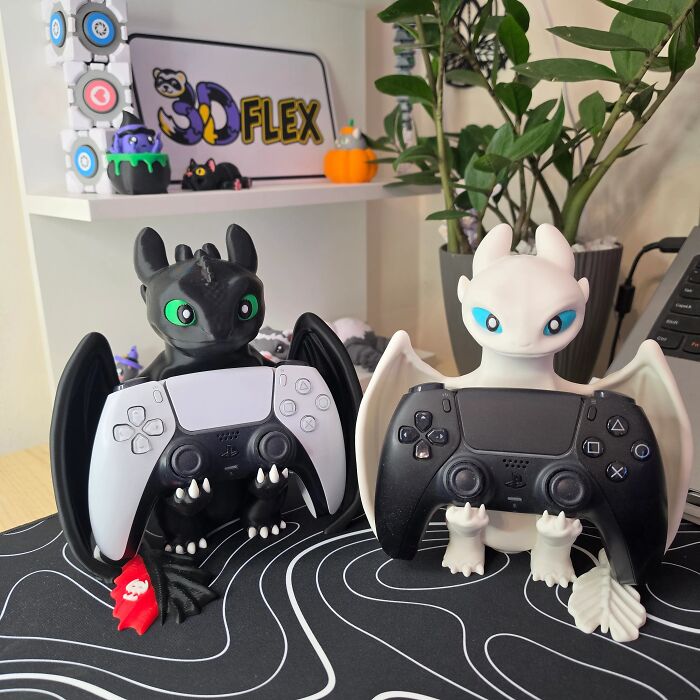 A pair of Toothless and Light Fury 3D prints used as game controller holders on a desk.