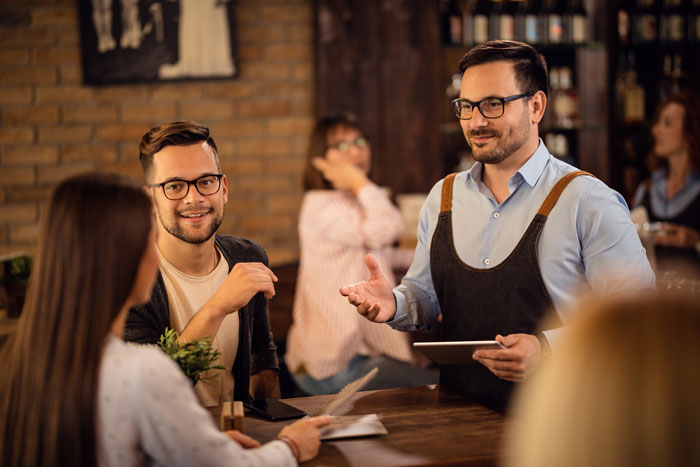 A waiter in a blue shirt and black apron taking an order at a restaurant A waiter in a blue shirt and black apron taking an order at a restaurant