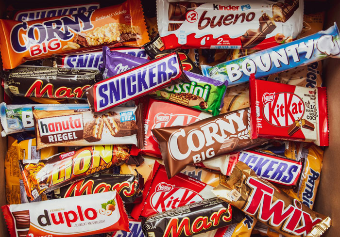 Assorted branded chocolate bars stacked in a pile, reflecting HOA Halloween candy regulations debate. Assorted branded chocolate bars stacked in a pile, reflecting HOA Halloween candy regulations debate.