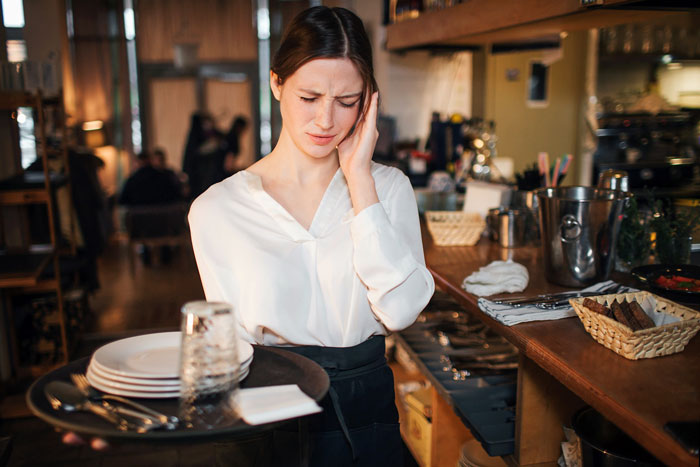 A stressed waiter with a headache holding a tray of plates and glasses A stressed waiter with a headache holding a tray of plates and glasses