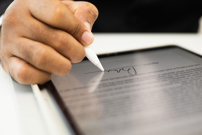 Close-up of hand signing a digital document on tablet with stylus pen