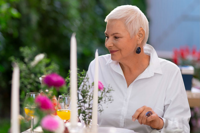 Woman with short white hair seated at a wedding table with floral decorations