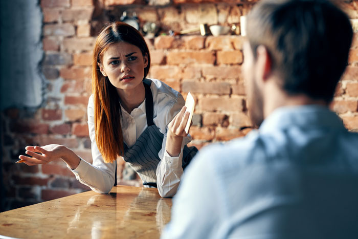 An annoyed waitress talks to a male customer, illustrating a bossy coworker scenario. An annoyed waitress talks to a male customer, illustrating a bossy coworker scenario.