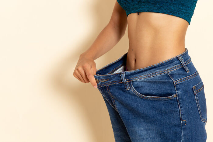 A fit woman holding out oversized jeans to demonstrate weight loss advice from doctors and nurses.