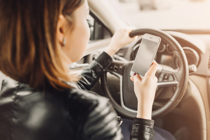 Woman holding a smartphone behind the wheel of a car, depicting driver safety and emergency tips.