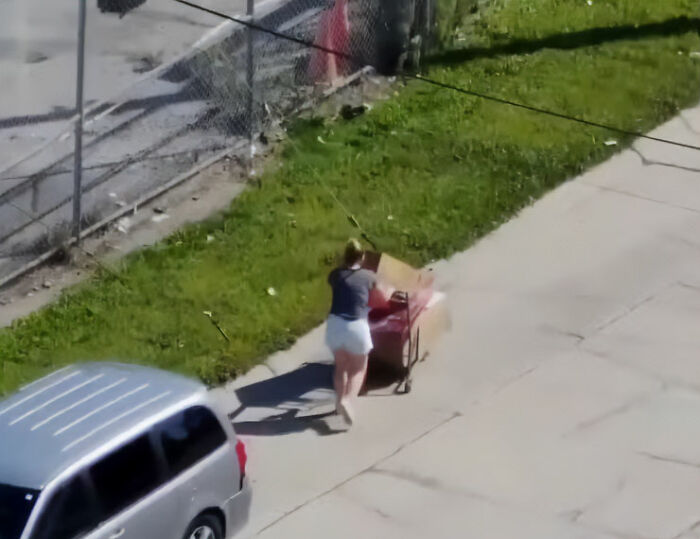 Woman pushing shopping cart on sidewalk near fence with Halloween decorations Woman pushing shopping cart on sidewalk near fence with Halloween decorations