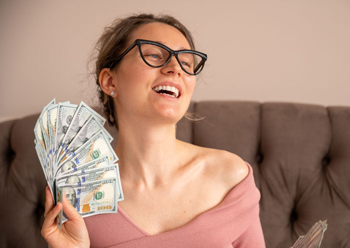 A smiling woman holding a fan of cash, representing financial gain mentioned in divorce stories.