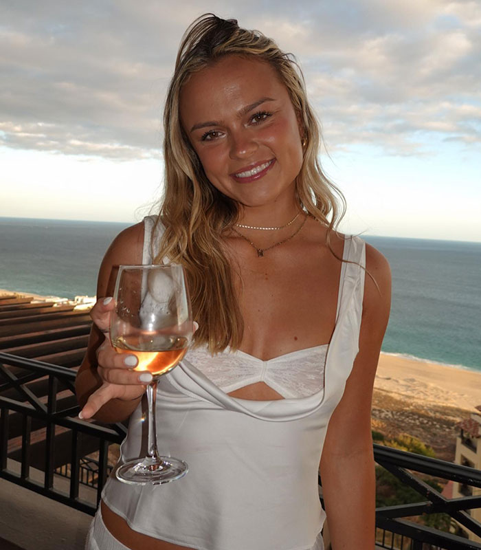 Woman holding wine glass with ocean view in casual white top