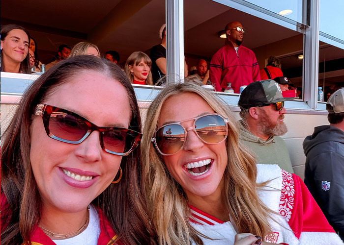 Two women smiling in front of Taylor Swift at the Chiefs game Two women smiling in front of Taylor Swift at the Chiefs game