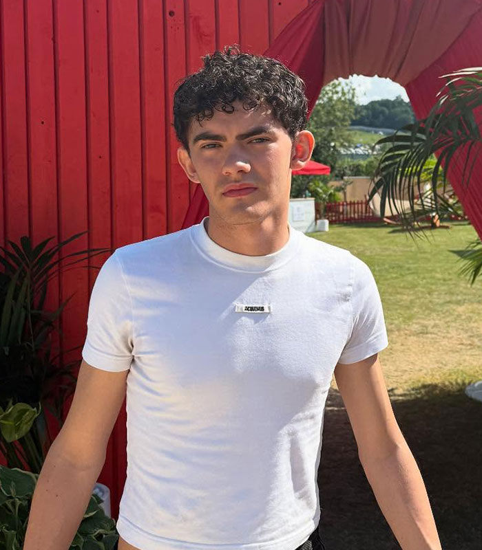 Hollywood star accused of cheating in white t-shirt standing outdoors near red wall