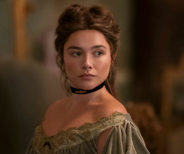 Florence Pugh wearing a velvet dress and black choker necklace in a period drama scene.
