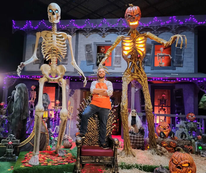 Man posing with giant Halloween skeleton and pumpkin decorations Man posing with giant Halloween skeleton and pumpkin decorations