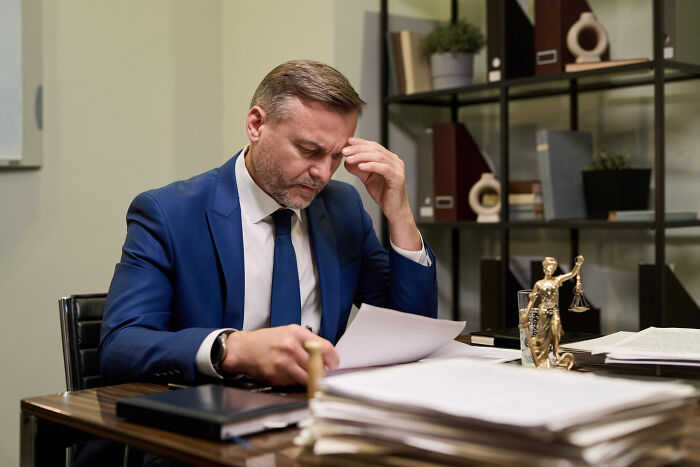 Stressed businessman in a blue suit at his desk, approaching his breaking point moments with paperwork.