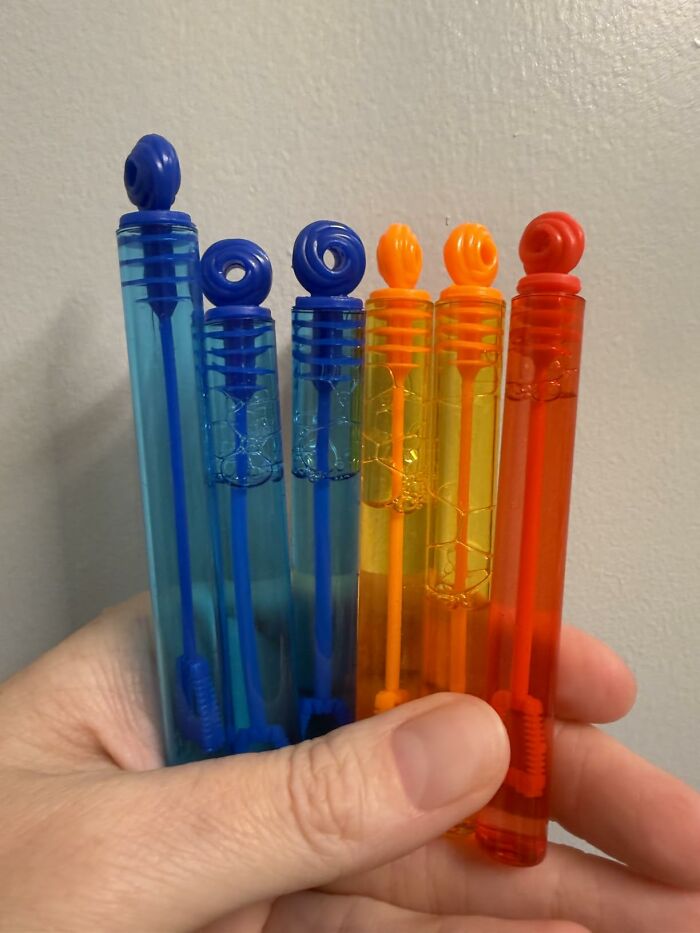Hand holding blue, yellow, and red bubble wands as Halloween treats