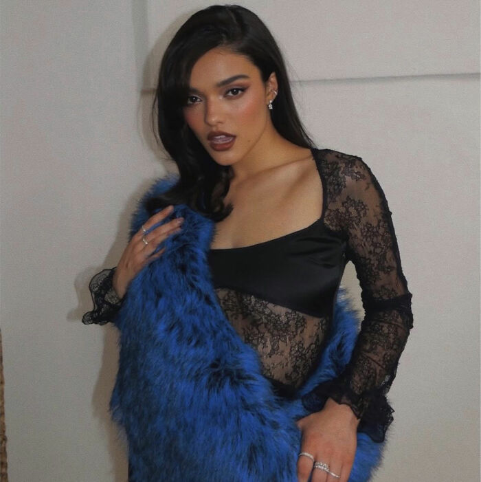 Rachel Zegler posing in a stylish black lace top and a bright blue faux fur wrap.