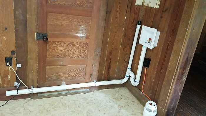 Poorly installed plumbing and drain pipe running across a wooden door in a DIY home improvement attempt.