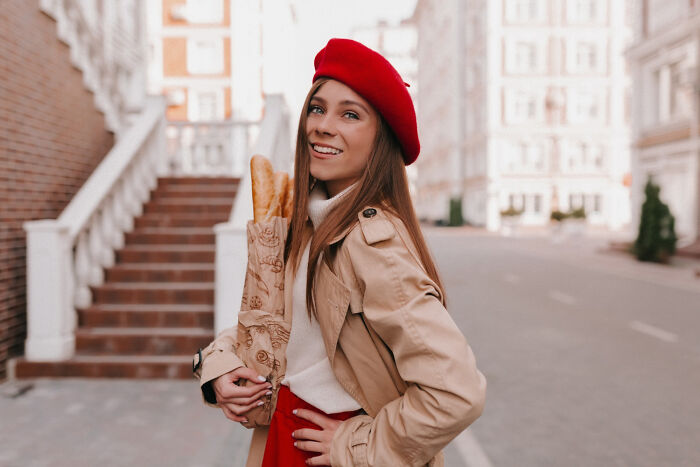 A stylish woman wearing a red beret holding french bread, looking like an obvious lie.