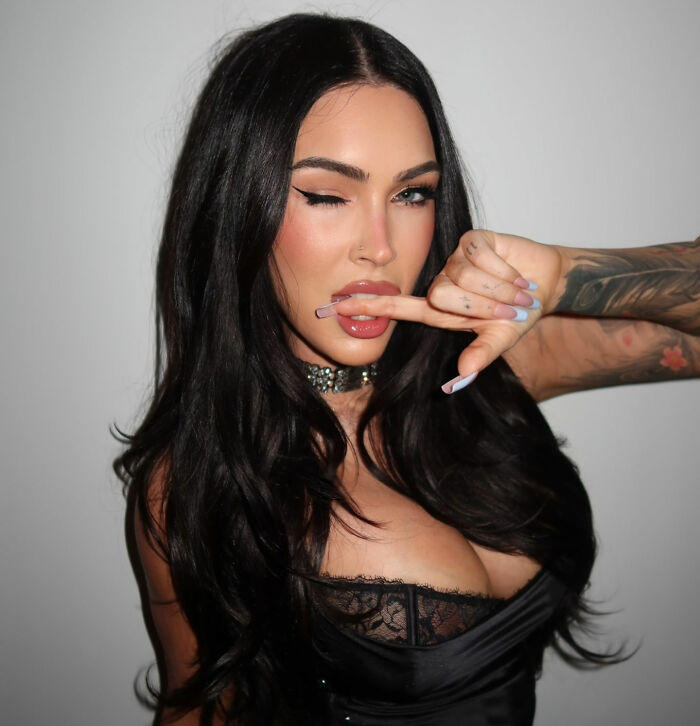 Megan Fox with dark hair winking and biting her finger, showing her distinct appearance. Megan Fox with dark hair winking and biting her finger, showing her distinct appearance.