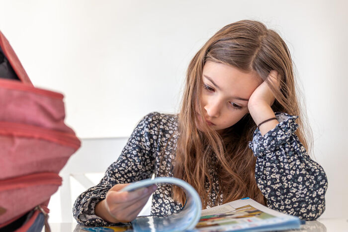 Bored student leaning on her hand while reading a textbook