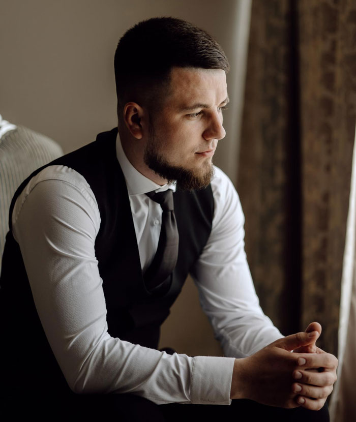 Groom wearing a vest and tie sitting thoughtfully before wedding ceremony