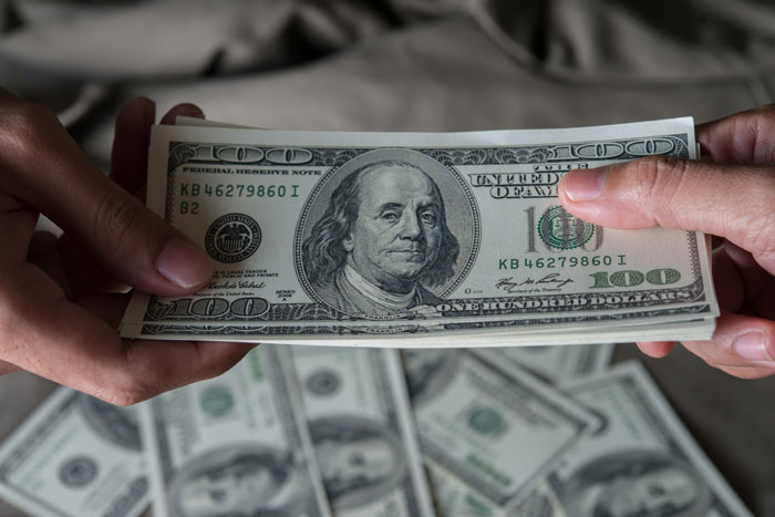 Hands holding a stack of US dollar bills for a honest school fundraiser