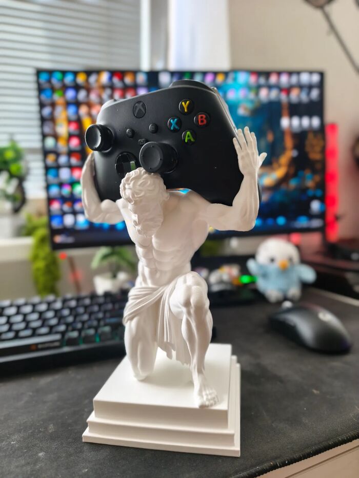 An Atlas-style white 3D print holding up an Xbox controller on a gaming desk.