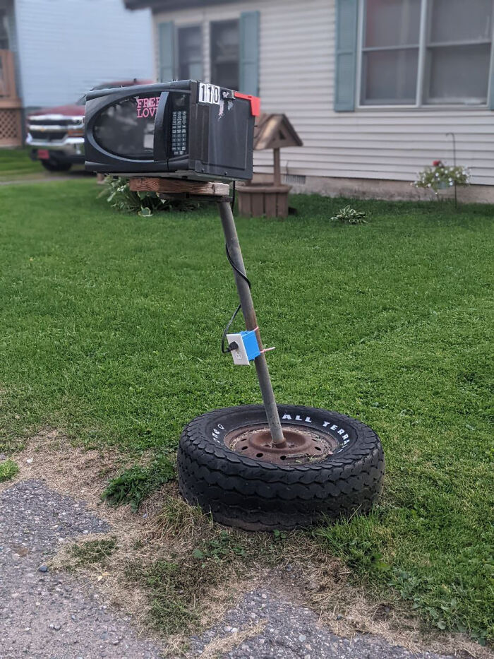 A creative DIY project showing a mailbox made from an old microwave on a post inside a tire.