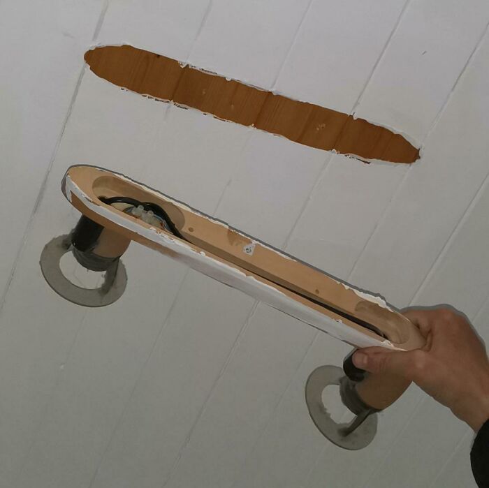 A hand holding a ceiling light fixture with an incorrect oblong hole cut during DIY projects.