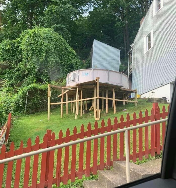An above ground pool awkwardly elevated on wooden stilts, showing a DIY project gone wrong