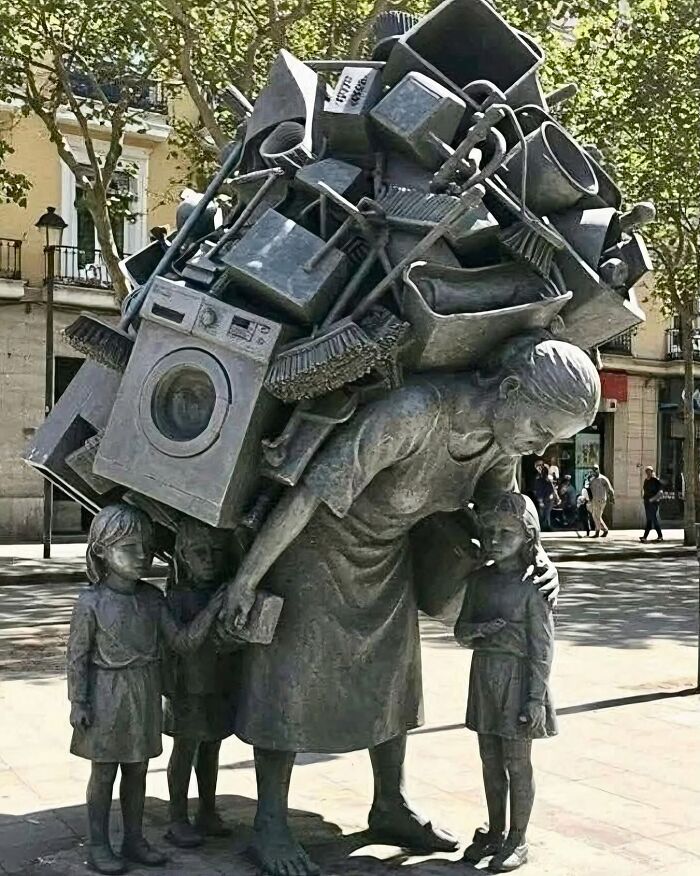 A cool statue of a mother carrying household chores on her back while holding her kids' hands.