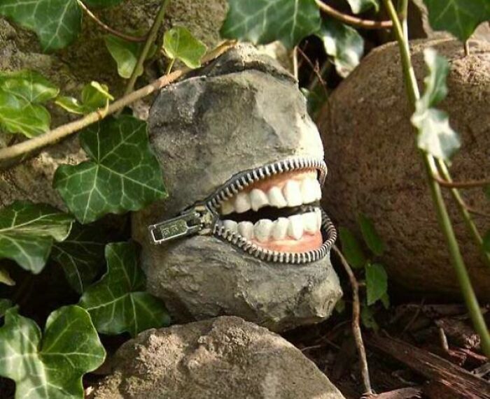 Bizarre DIY Projects stone sculpture with a metal zipper mouth revealing realistic human teeth among green ivy