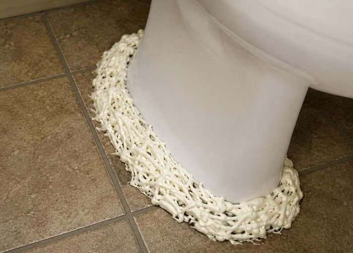 A poorly executed DIY project showing thick, messy polyurethane expanding foam sealed around a toilet base on floor tiles