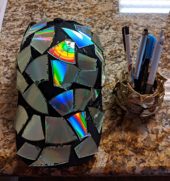 Unique DIY Projects black cap covered in shiny mosaic pieces of broken CDs next to a decorative pen holder