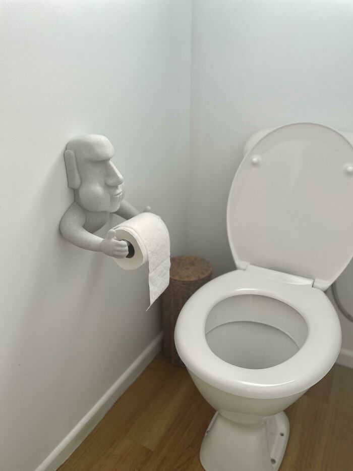 An Easter Island Moai head toilet paper holder mounted on a wall, depicting custom 3D prints.
