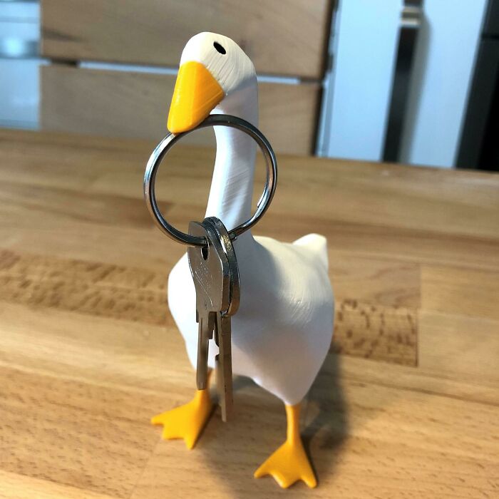 A funny 3D prints white goose holding a ring with keys in its orange beak.