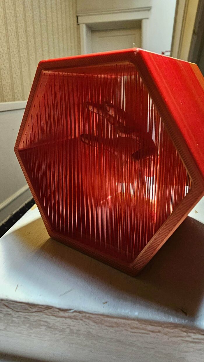 A red hexagonal lamp with delicate 3D prints vertical lines casting light.