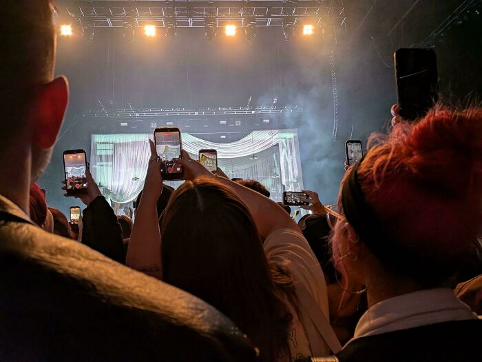 A crowd at a concert holding up smartphones to record, a common scene in modern life in America.