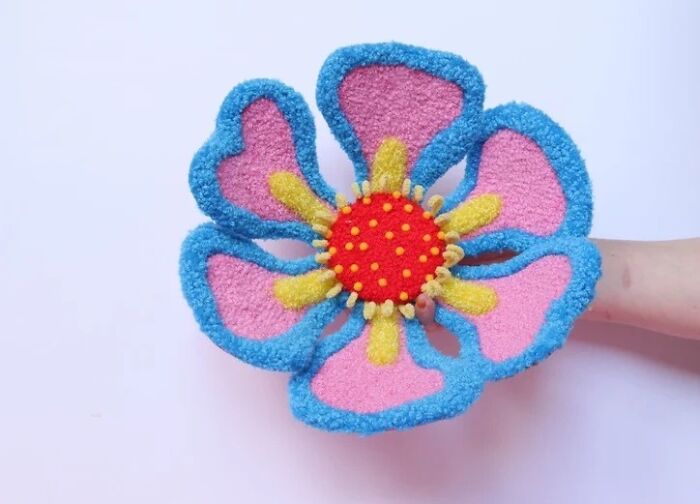 Handcrafted pink and blue tufted flower textile art piece held up by Ina Dyreborg.