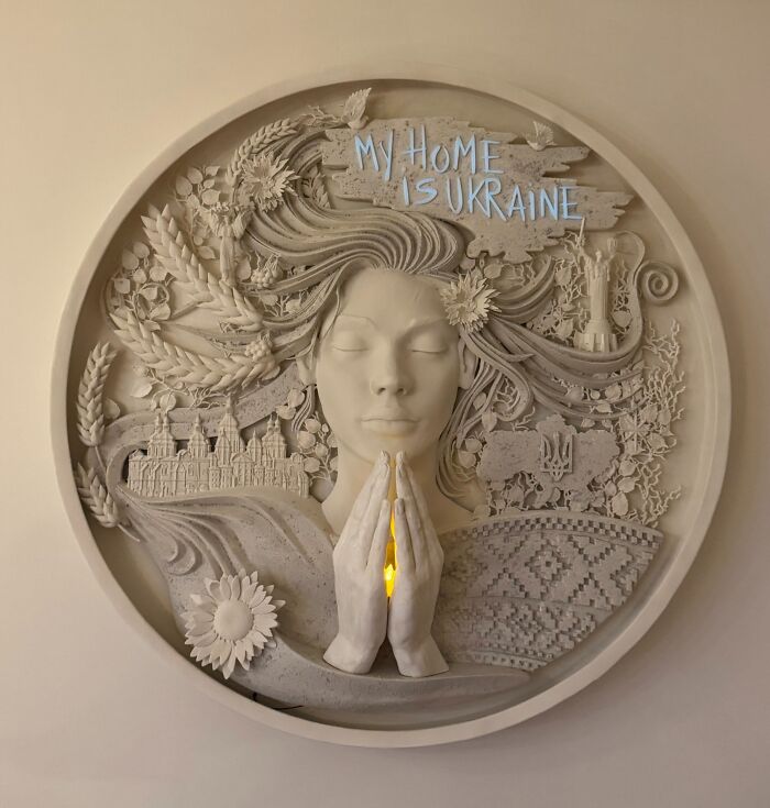 An intricate circular wall relief sculpture made from 3D prints depicting a praying woman and Ukrainian symbols.
