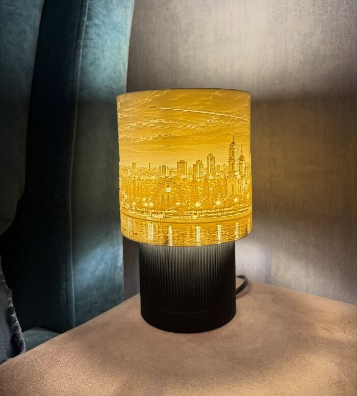 A detailed 3D prints lampshade depicting a golden city skyline silhouette glowing warmly.