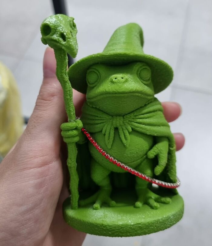 A hand holding a green wizard frog figurine created with 3D prints.
