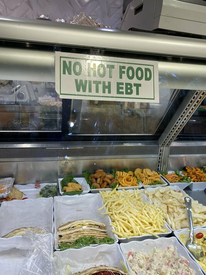 Delicatessen counter sign stating No Hot Food With EBT, reflecting modern life in America assistance policies.