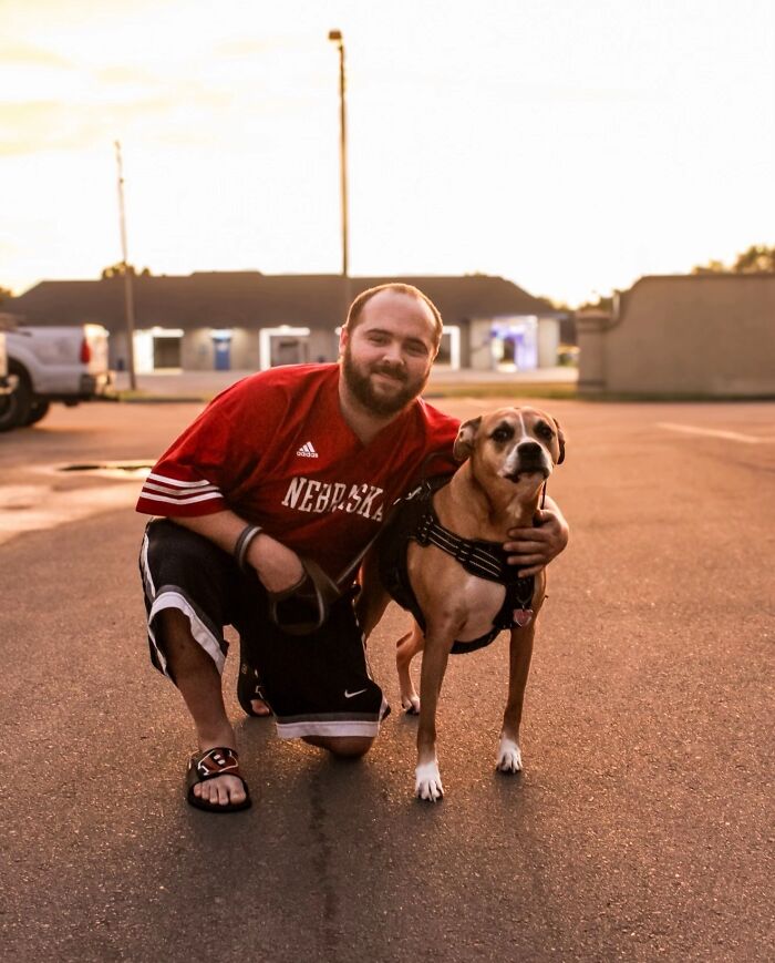 A man in a red jersey kneeling with his dog, sharing life stories with pets.