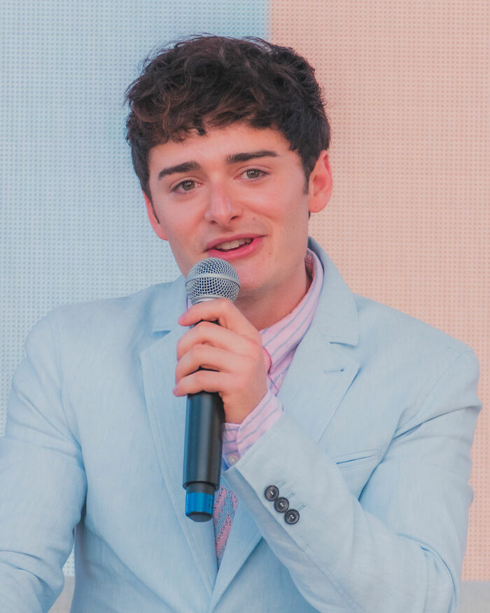 Noah Schnapp speaking into a microphone while wearing a light blue suit jacket