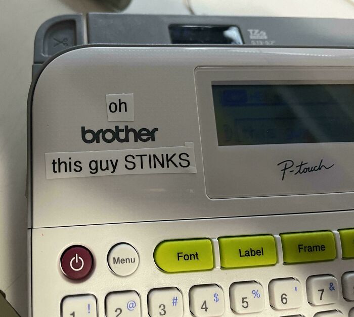 Clever vandalism on a label maker machine with a sticker joke saying oh brother this guy stinks.