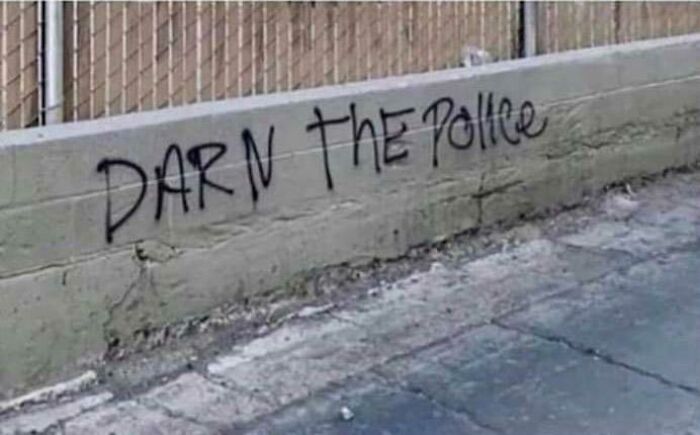 Vandalism on a concrete wall with black spray paint reading Darn the Police as a polite act of public art