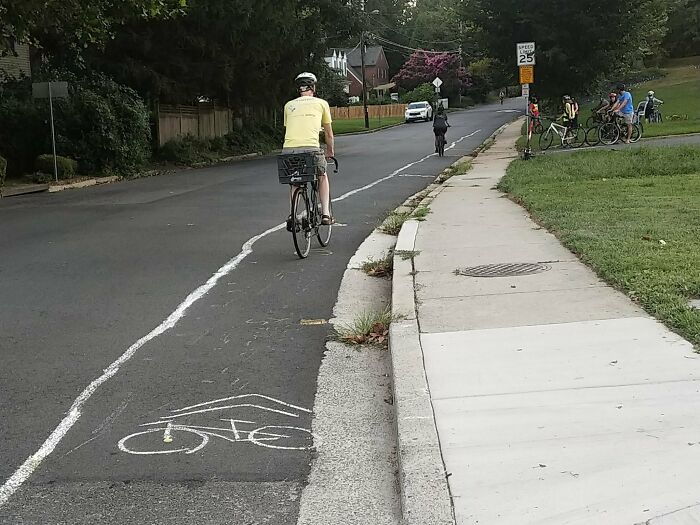 A hand-painted bike lane line that curves around a cyclist, showing a creative act of vandalism