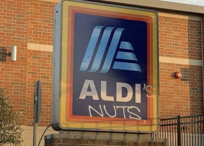 An Aldi store sign humorously vandalized with spray paint, displaying a funny act of vandalism as public art.