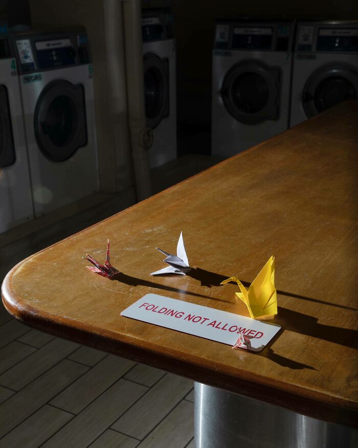 Paper cranes on laundry table over a sign saying folding not allowed, a clever act of vandalism.